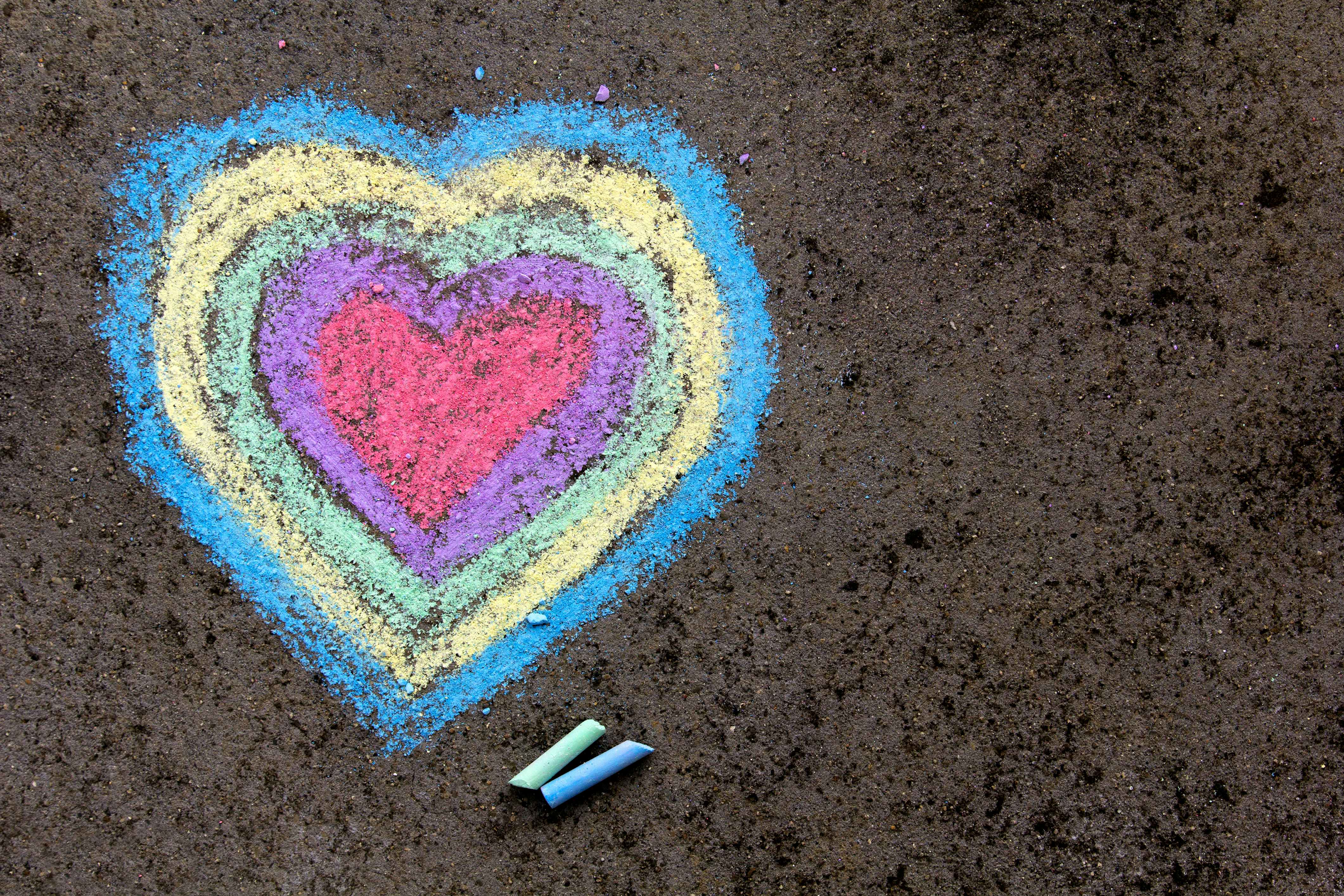 Multicolored chalk heart on pavement with two pieces of chalk next to it