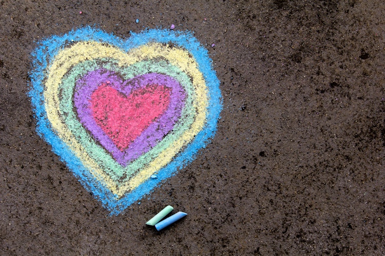 Multicolored chalk heart on pavement with two pieces of chalk next to it