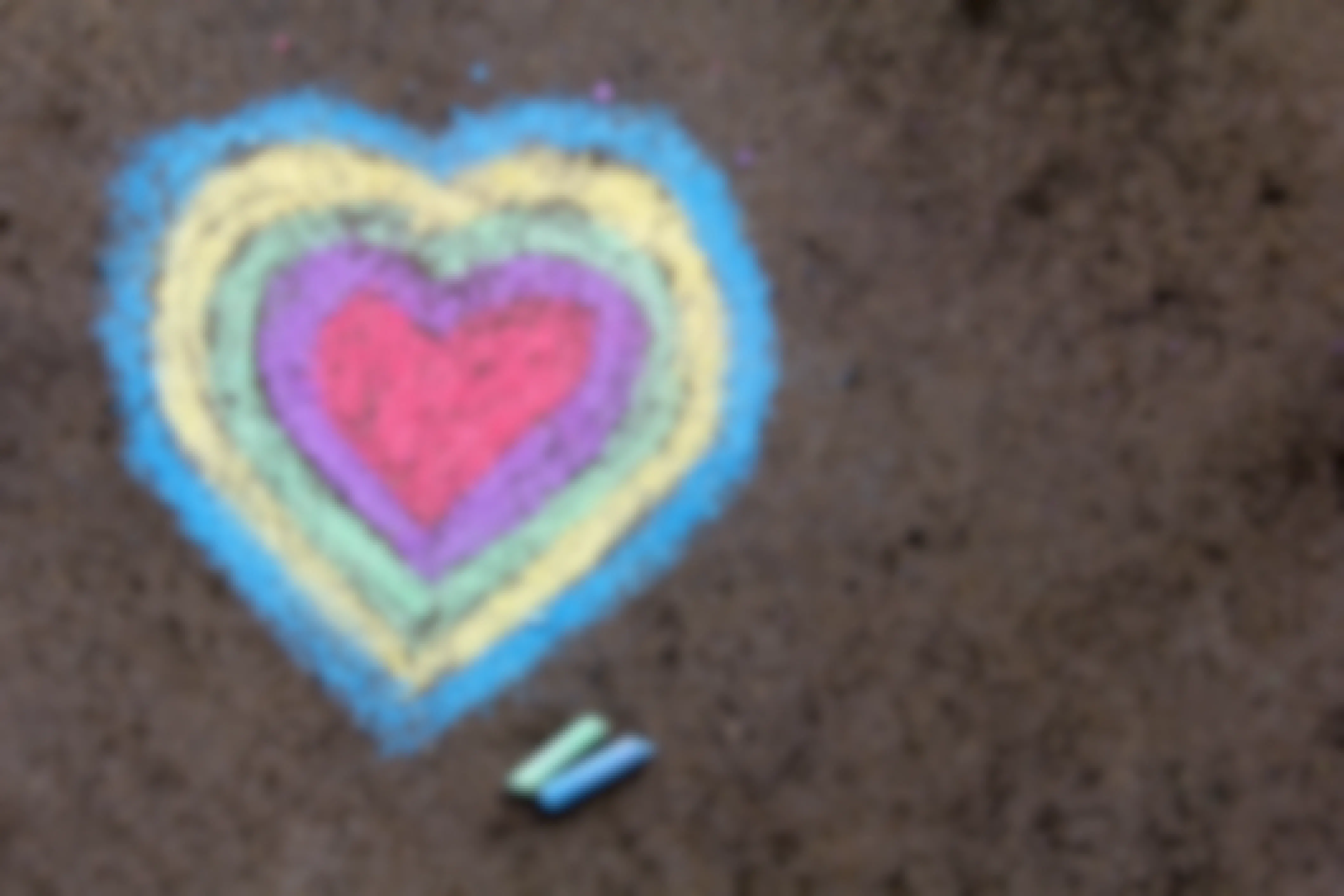 Multicolored chalk heart on pavement with two pieces of chalk next to it