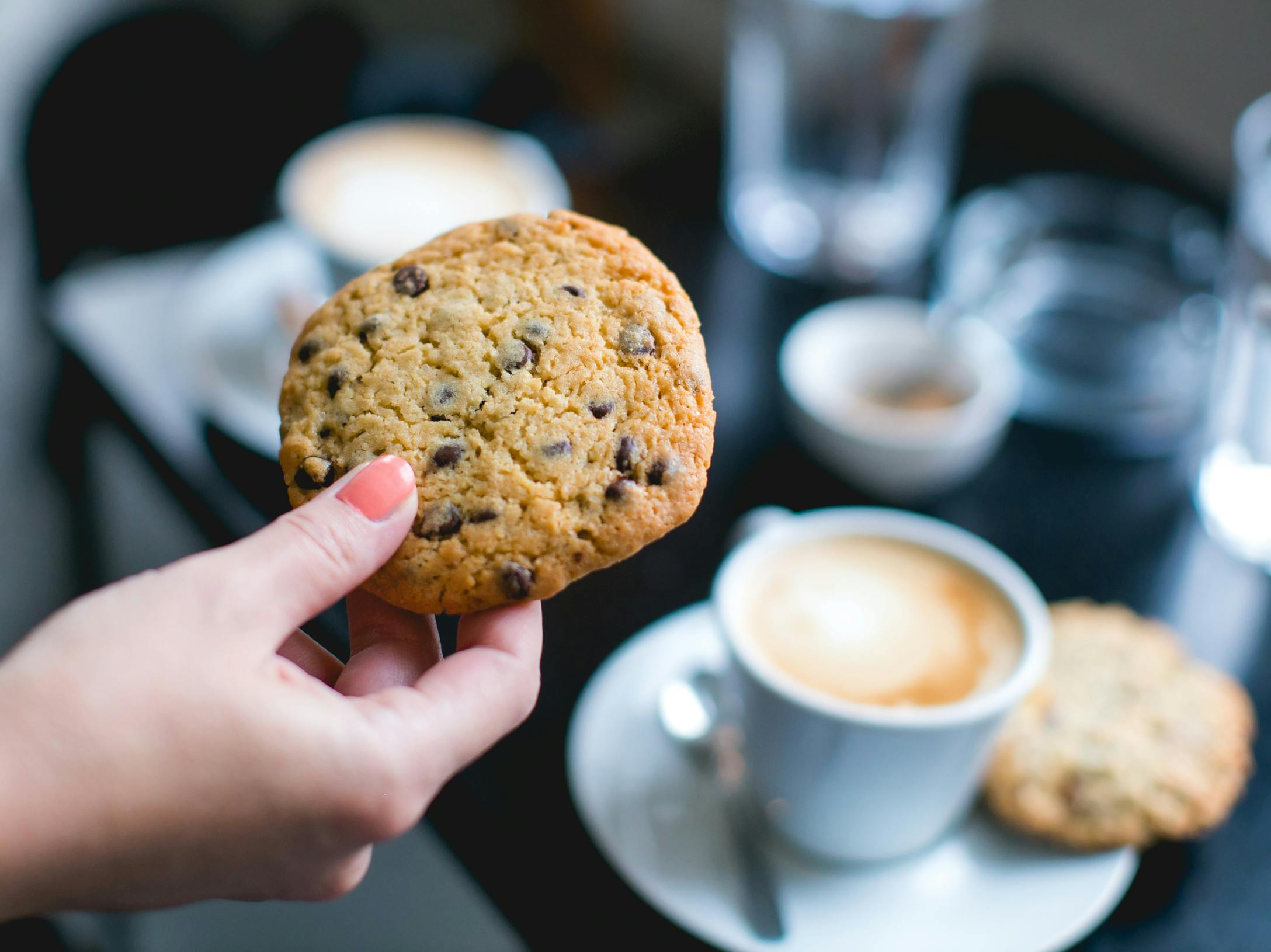 A person holding a cookie in front of a table in a restaurant or cafe