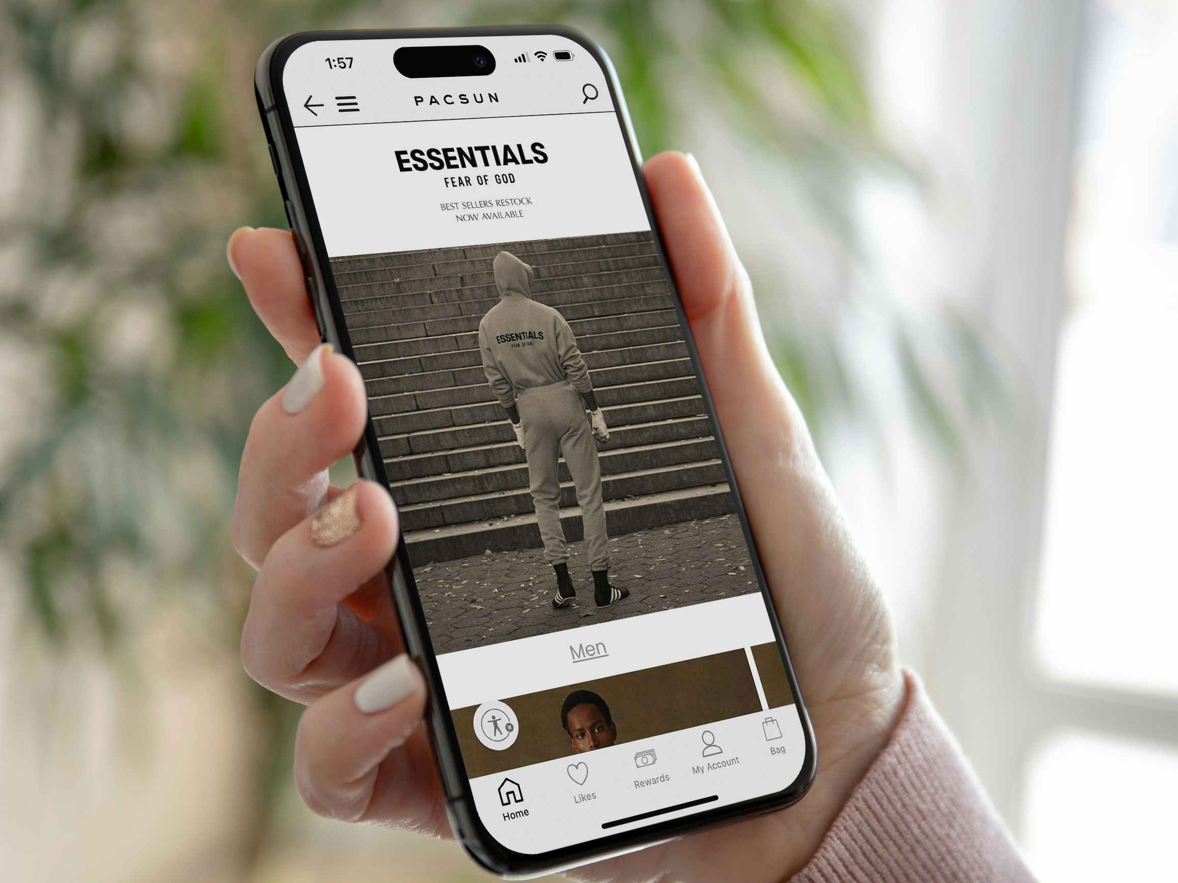 Someone holding a phone displaying the Essentials Fear of God brand page on the PacSun app