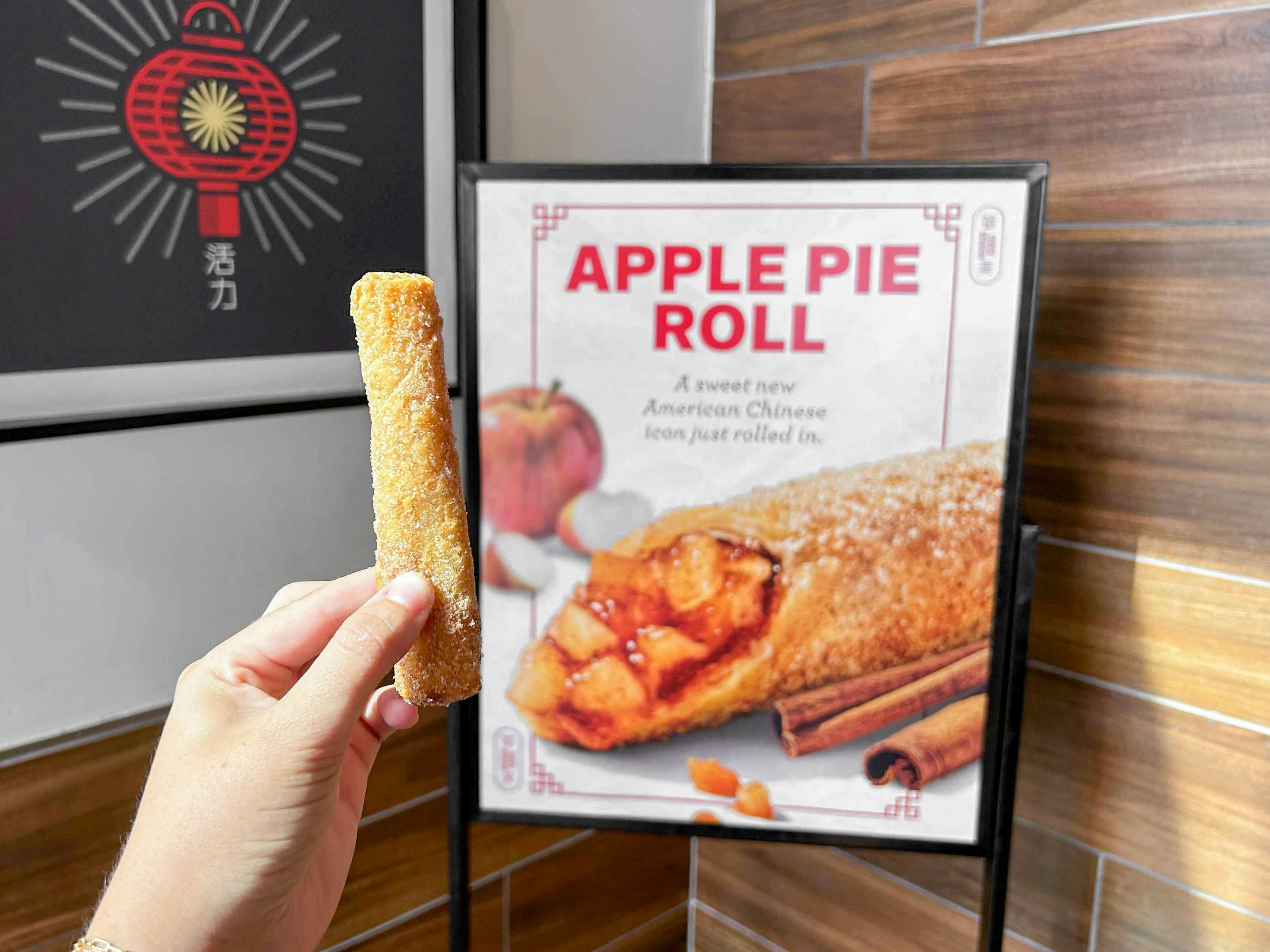 someone holding up an apple pie roll in front of a Panda Express sign