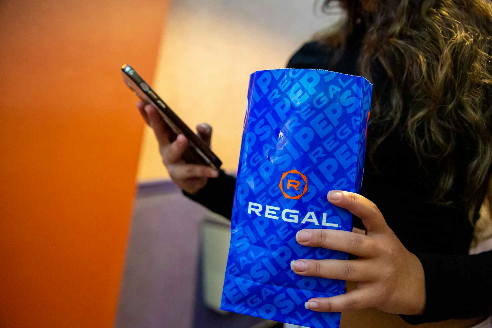 Woman holding a cellphone and a regal cinemas popcorn bag