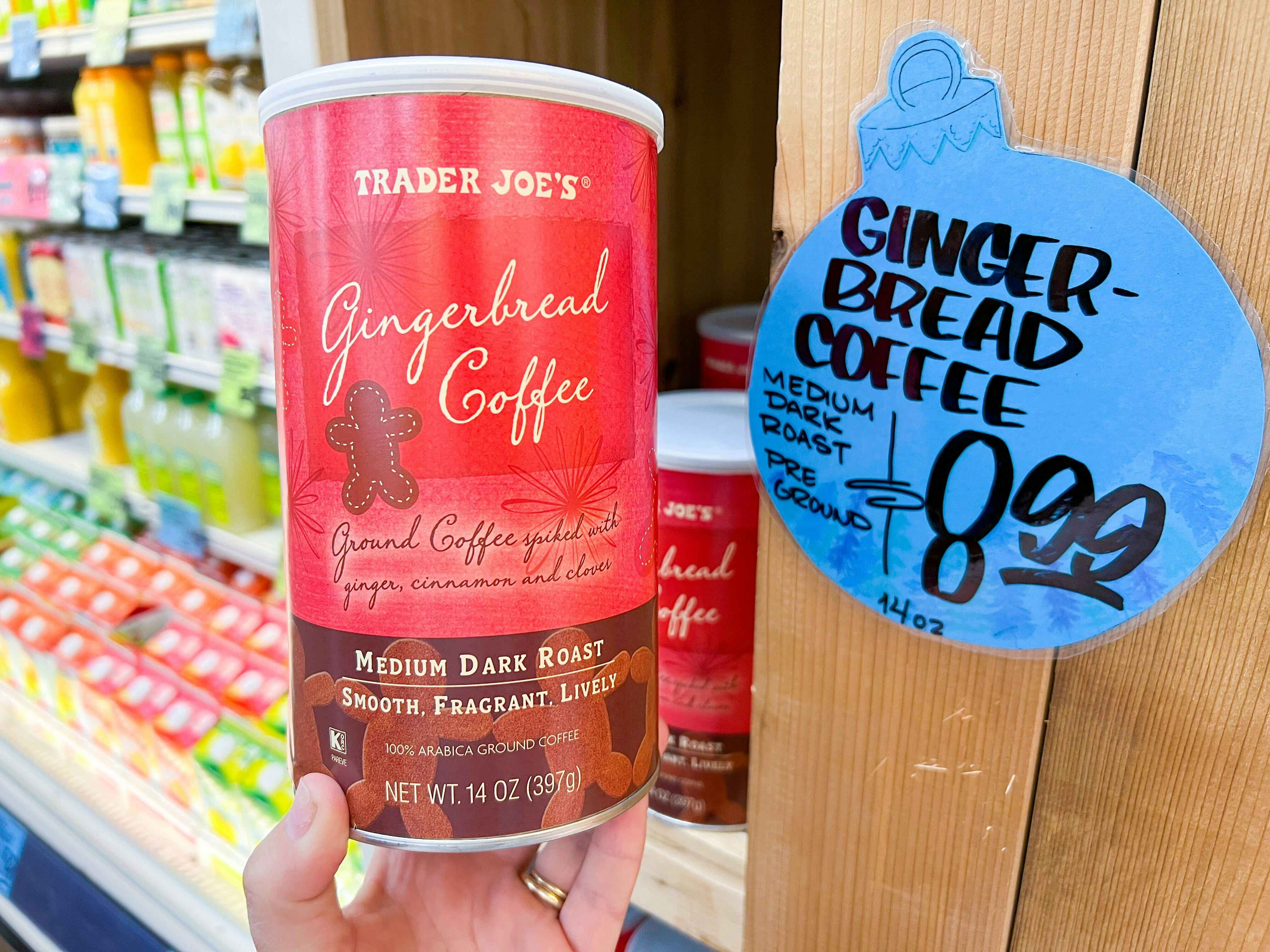 hand holding container of Trader Joe's Gingerbread Coffee in front of sign