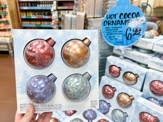 hand holding box of trader joe's hot coca ornaments in front of display in store