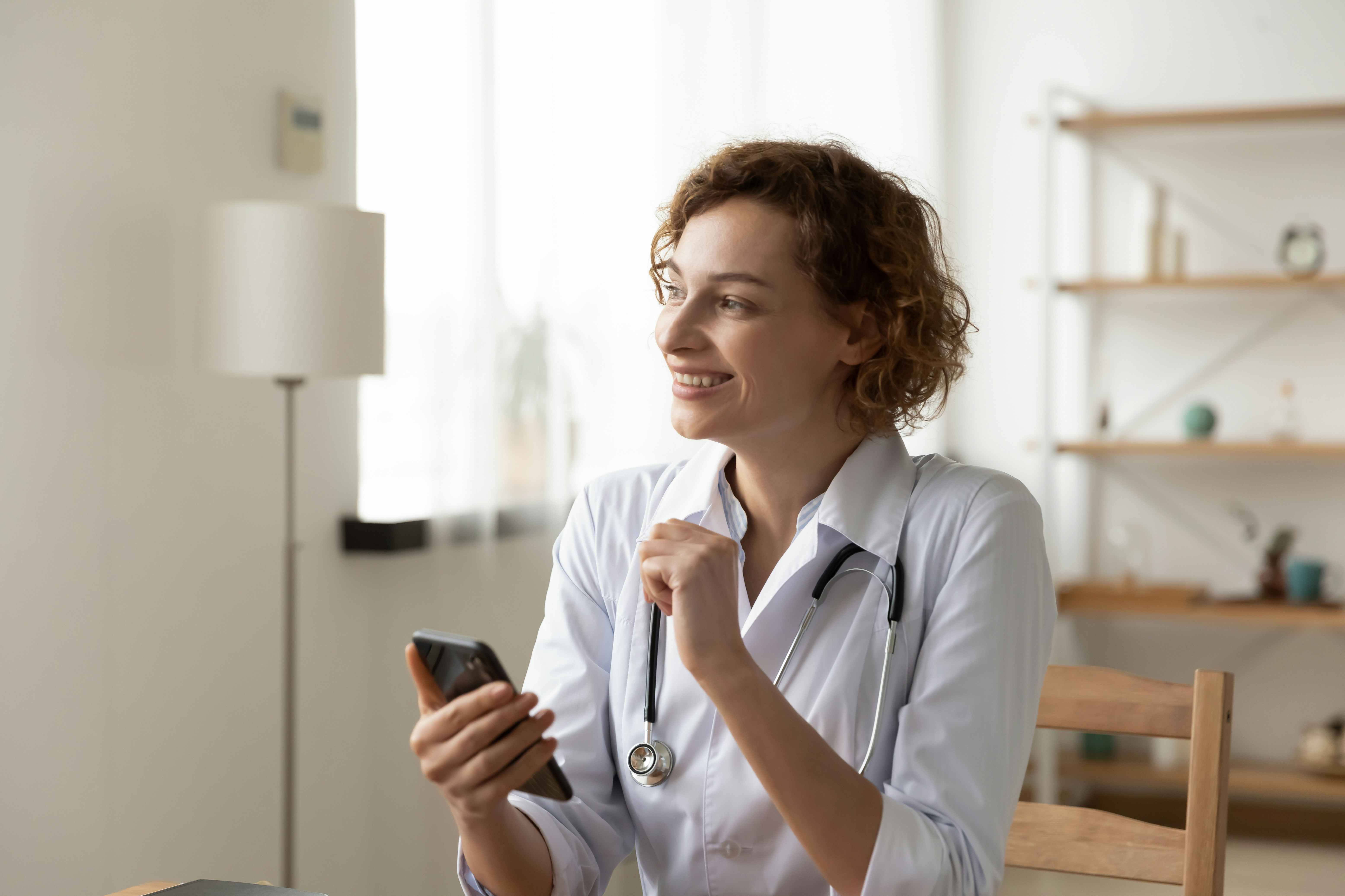 Doctor looking away from camera, as she holds her mobile phone