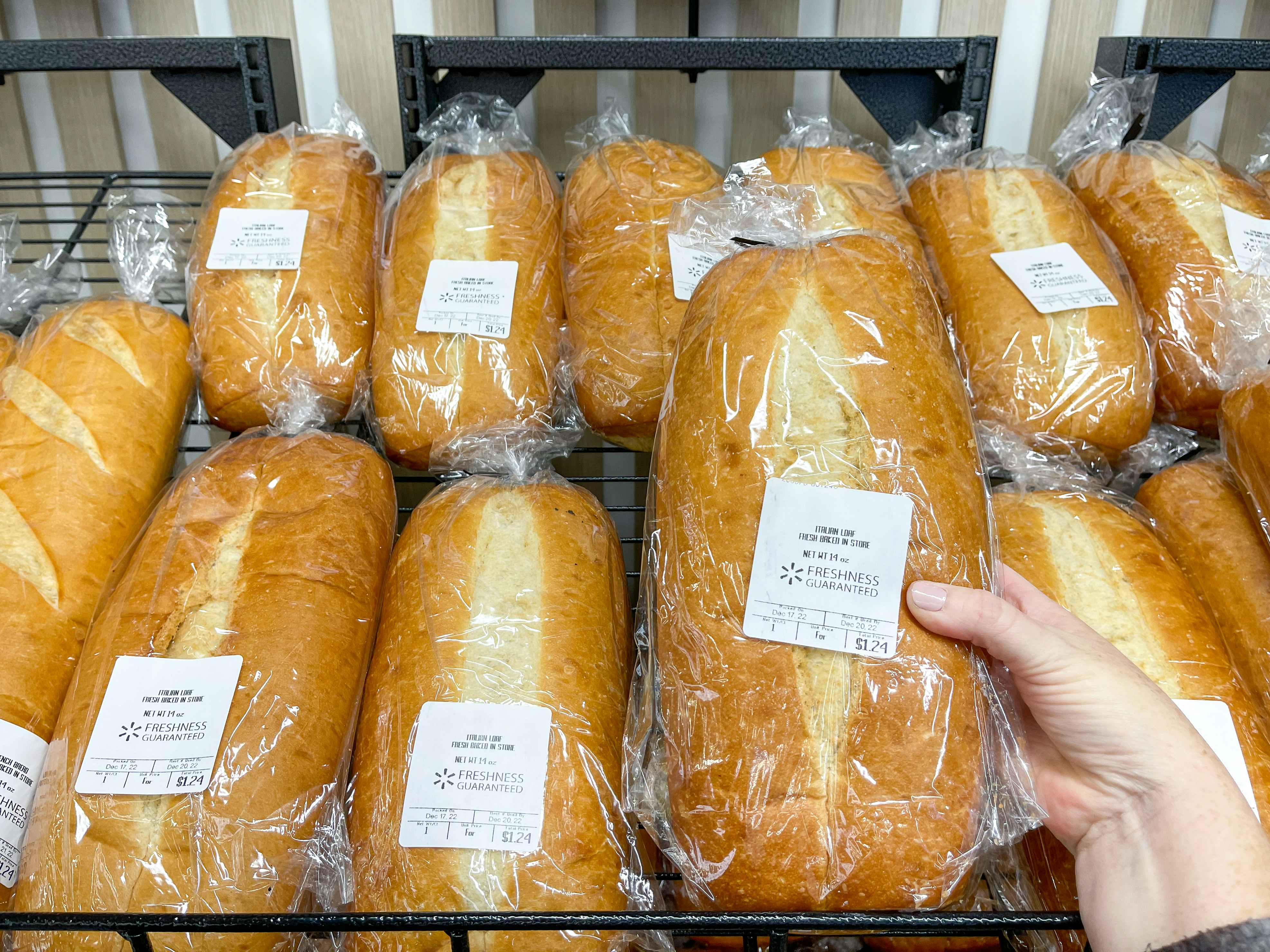 Someone picking out a loaf of bread from a shelf in the Walmart bakery section