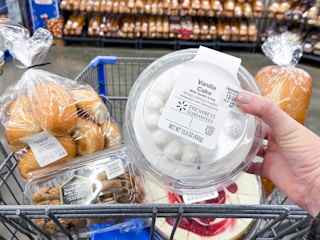 Someone putting a small cake into a Walmart shopping cart parked in the Walmart bakery