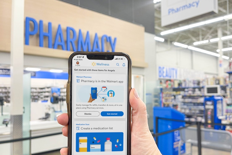 a person holding a phone with the walmart wellness app in front of the walmart pharmacy 