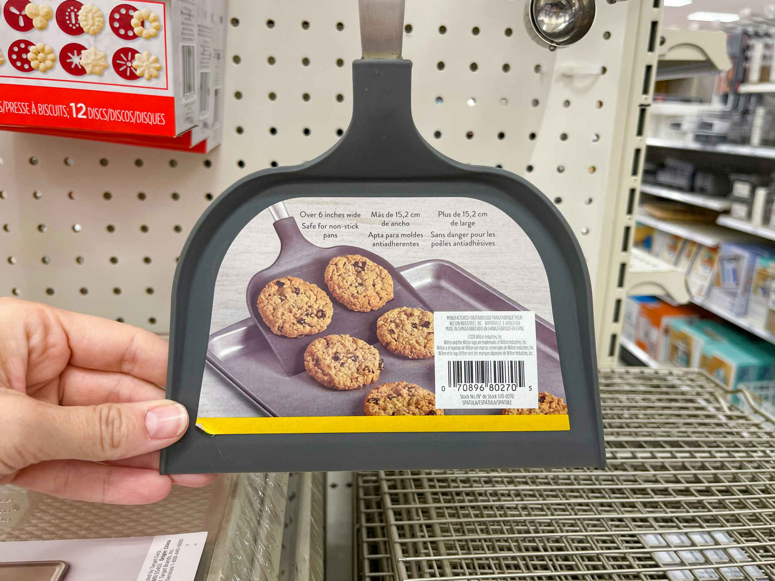 A Wilton Big Cookie Spatula held out by hand while it's hanging from a rack.