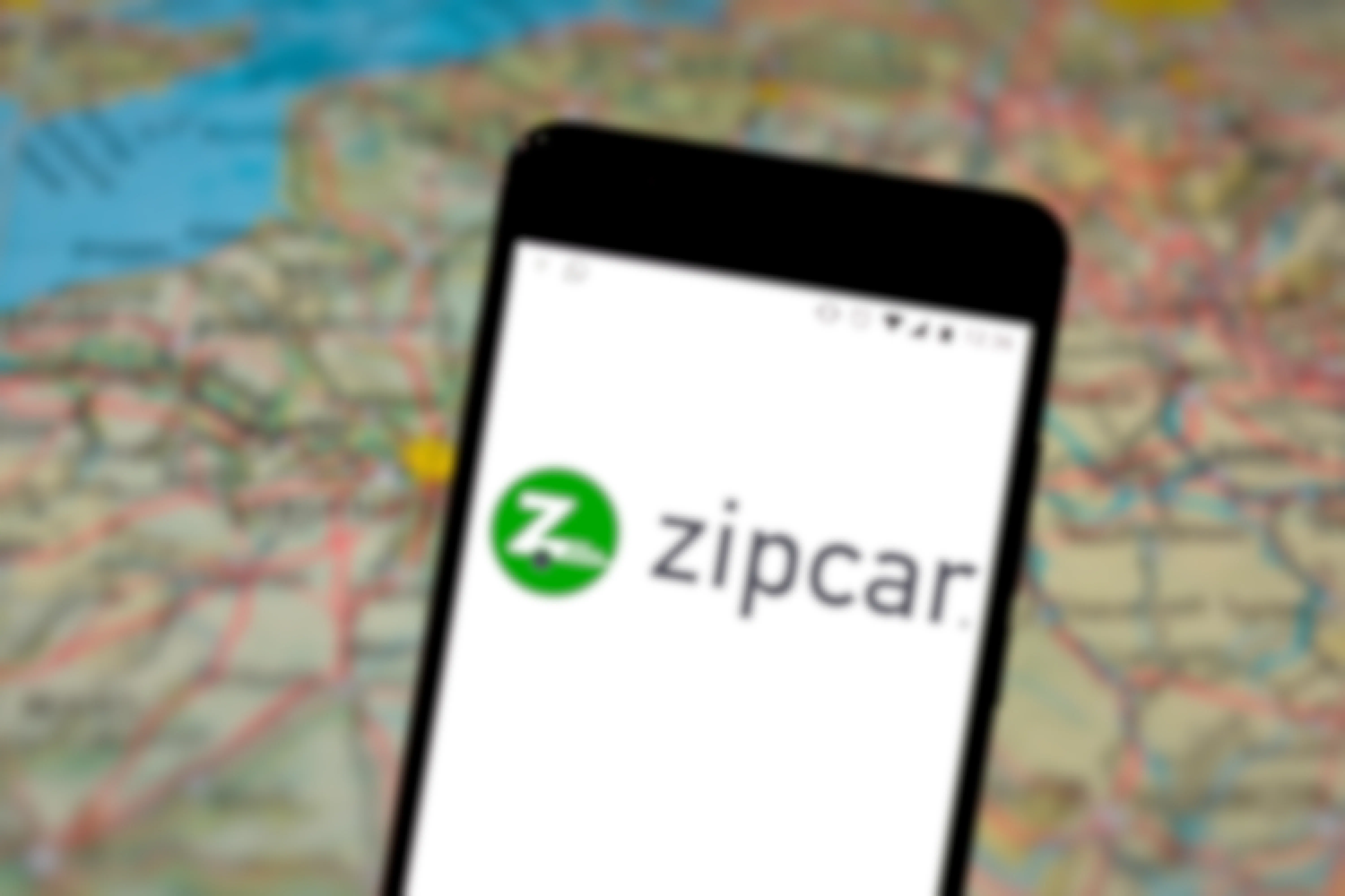 Zipcar logo on iphone with a blurred map as the background