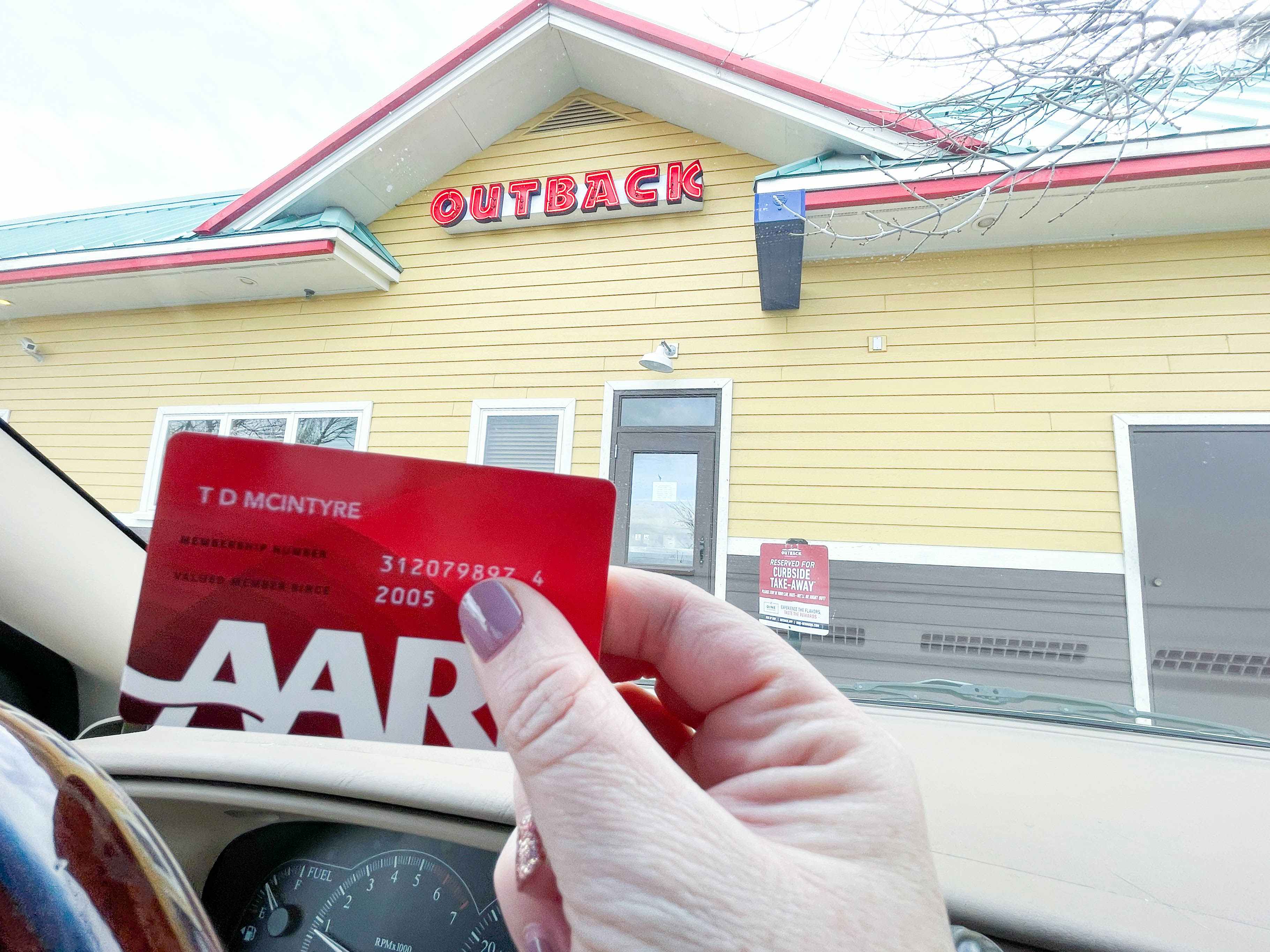 a person holding an aarp card while in a card outside outback steak house curbside 