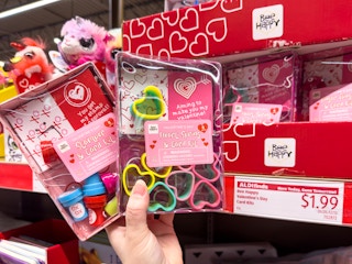 Someone holding Bee Happy Valentine's Day kits in front of their price tag at Aldi