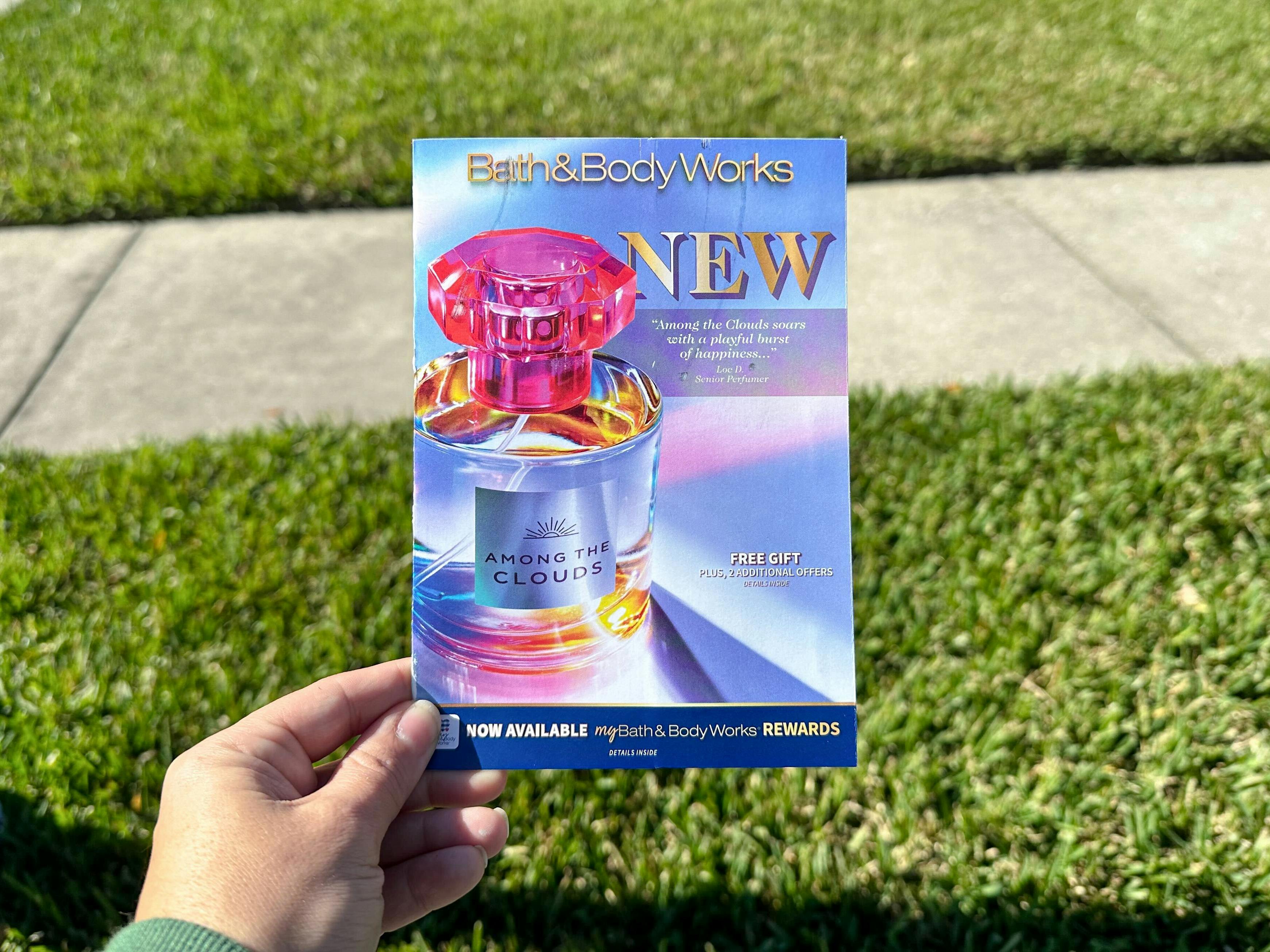 Someone holding a Bath & Body Works mailer coupon book in front of their lawn