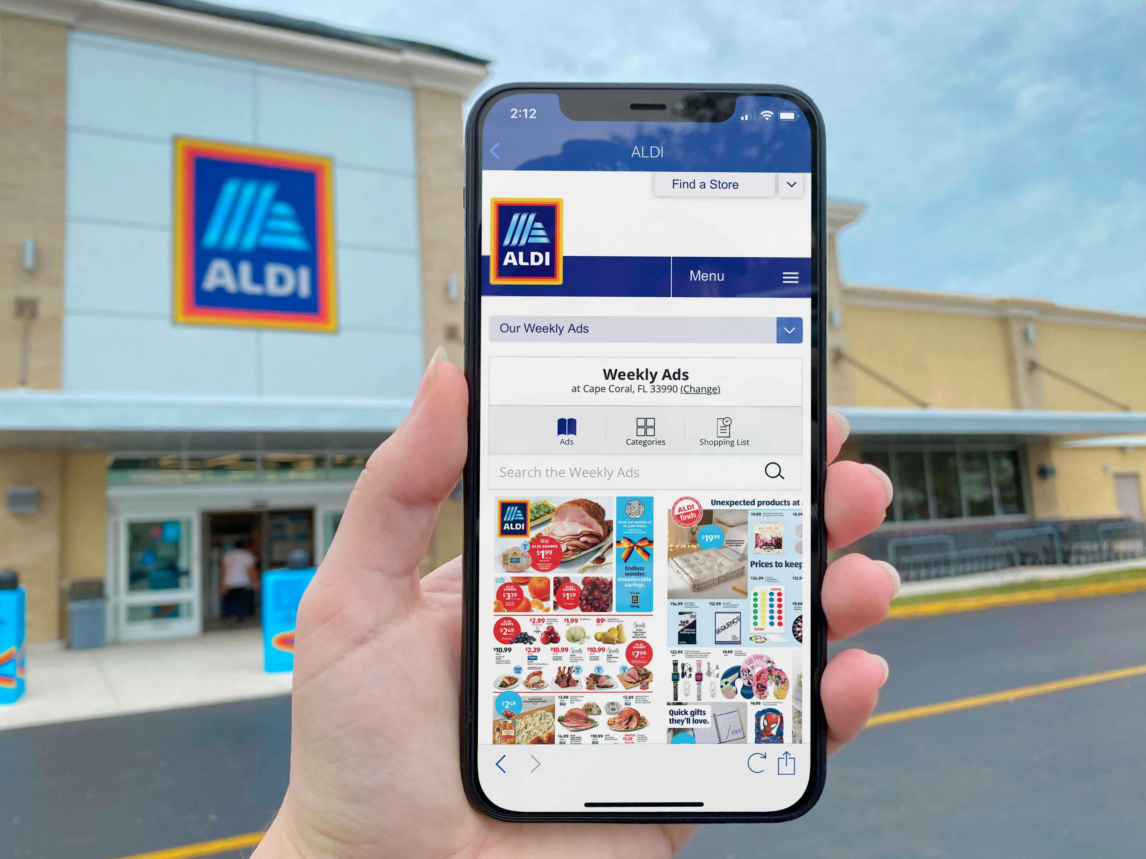 Someone holding up their phone displaying the Aldi app in front of an Aldi store