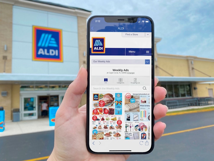 Someone holding up their phone displaying the Aldi app in front of an Aldi store