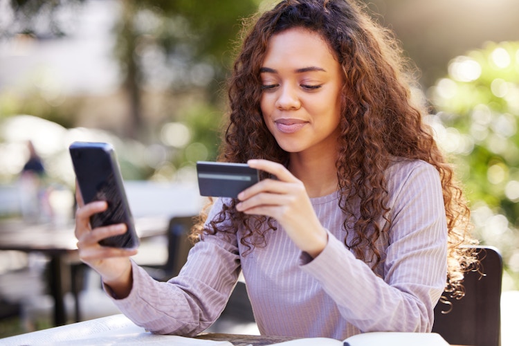 A college student holding a phone and looking at a credit card