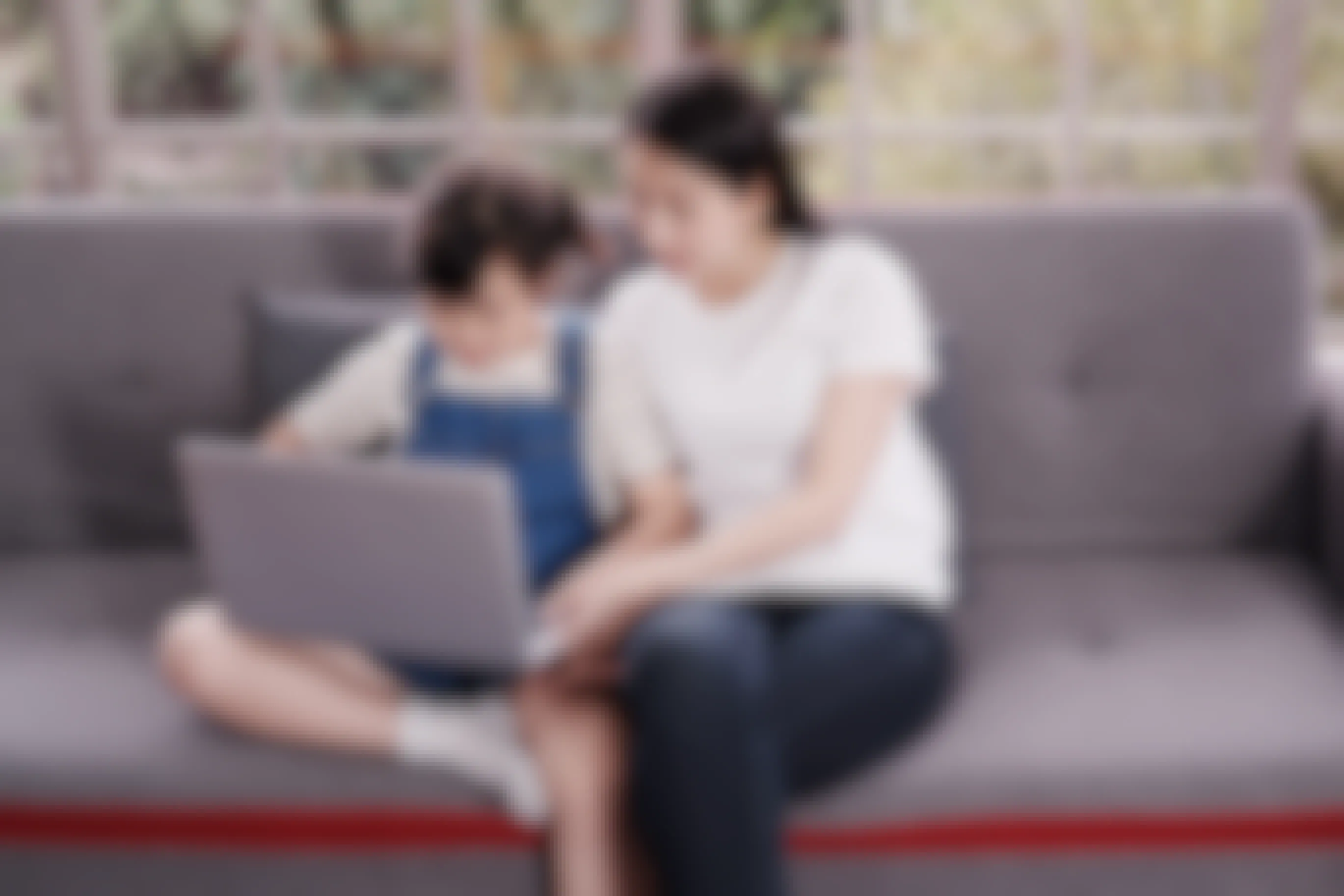 A child and parent looking at a laptop together on a couch