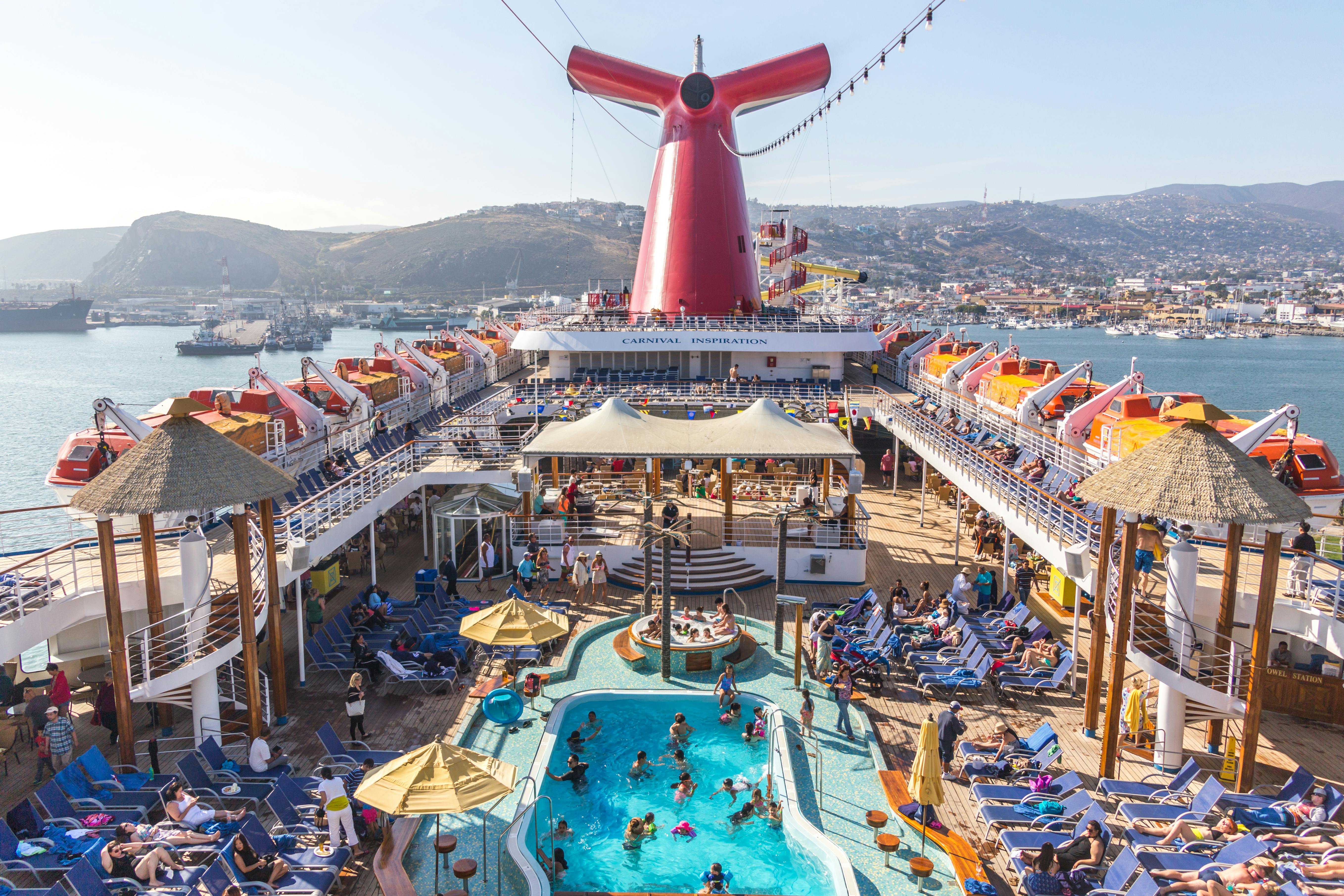 An inside view of a Carnival Cruise's upper deck, showing a pool, hot tub, and tons of other vacationers lounging in the area
