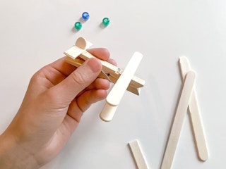 hand holding a diy clothespin and popsicle stick airplane craft