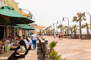 A view of the Myrtle Beach Boardwalk with people sitting to eat at an outdoor restaurant