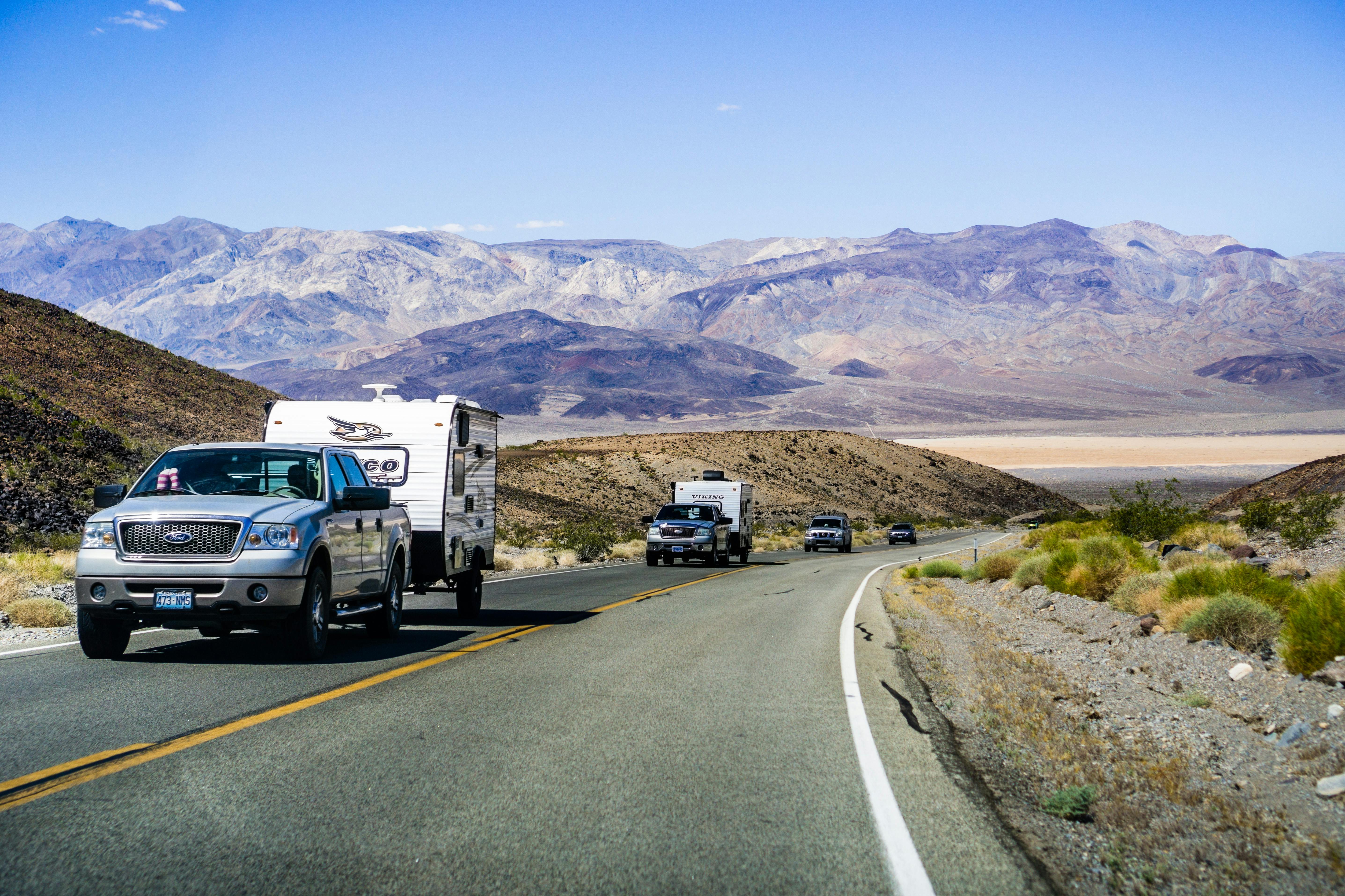 Two trucks towing RV campers driving up a hill with scenic mountains in the background