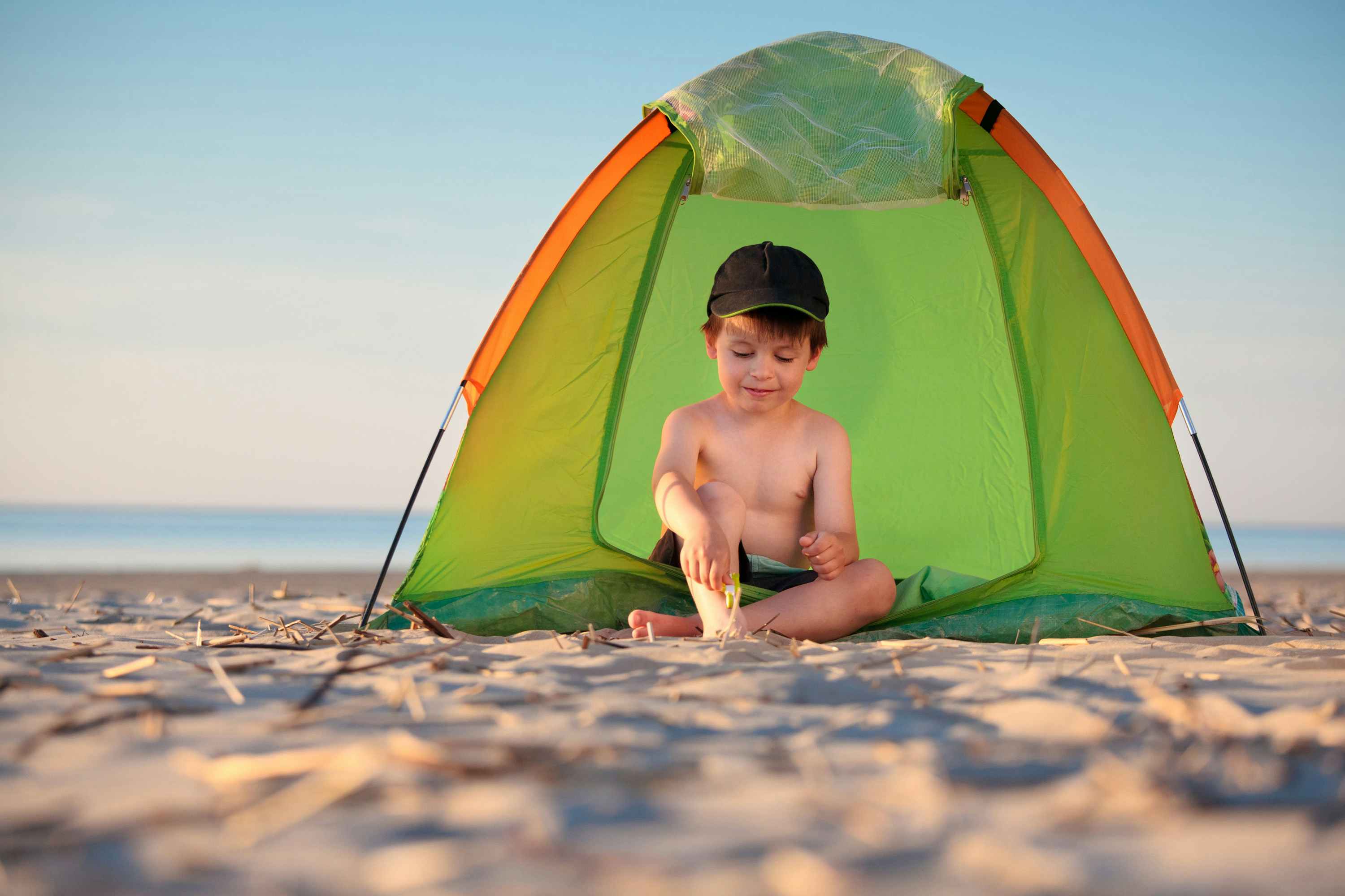 Child at a beach pplaying with sand under a small tent