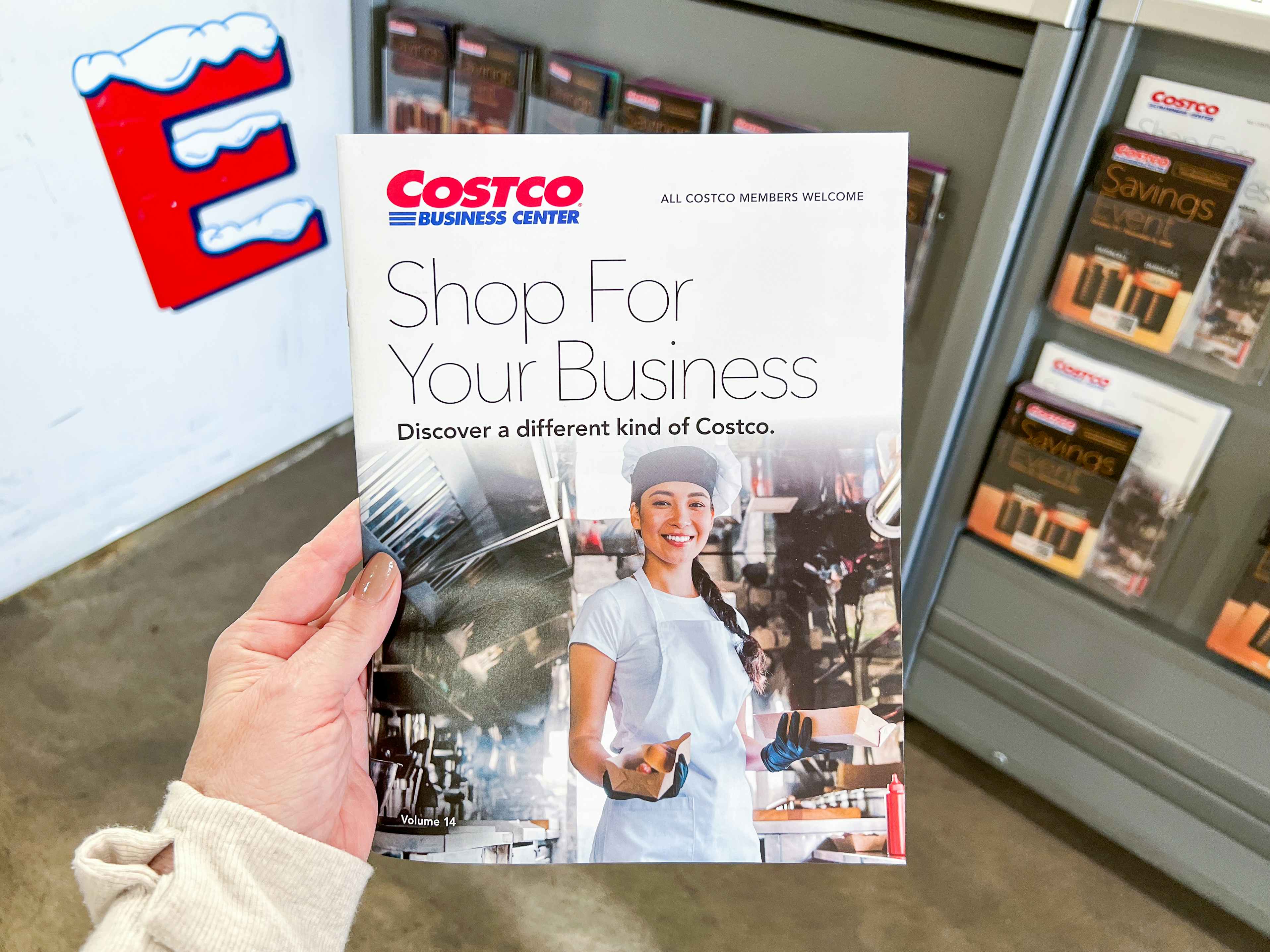 A person holding up a Costco Business Center booklet that says "Shop for your business" and "All Costco Members welcome