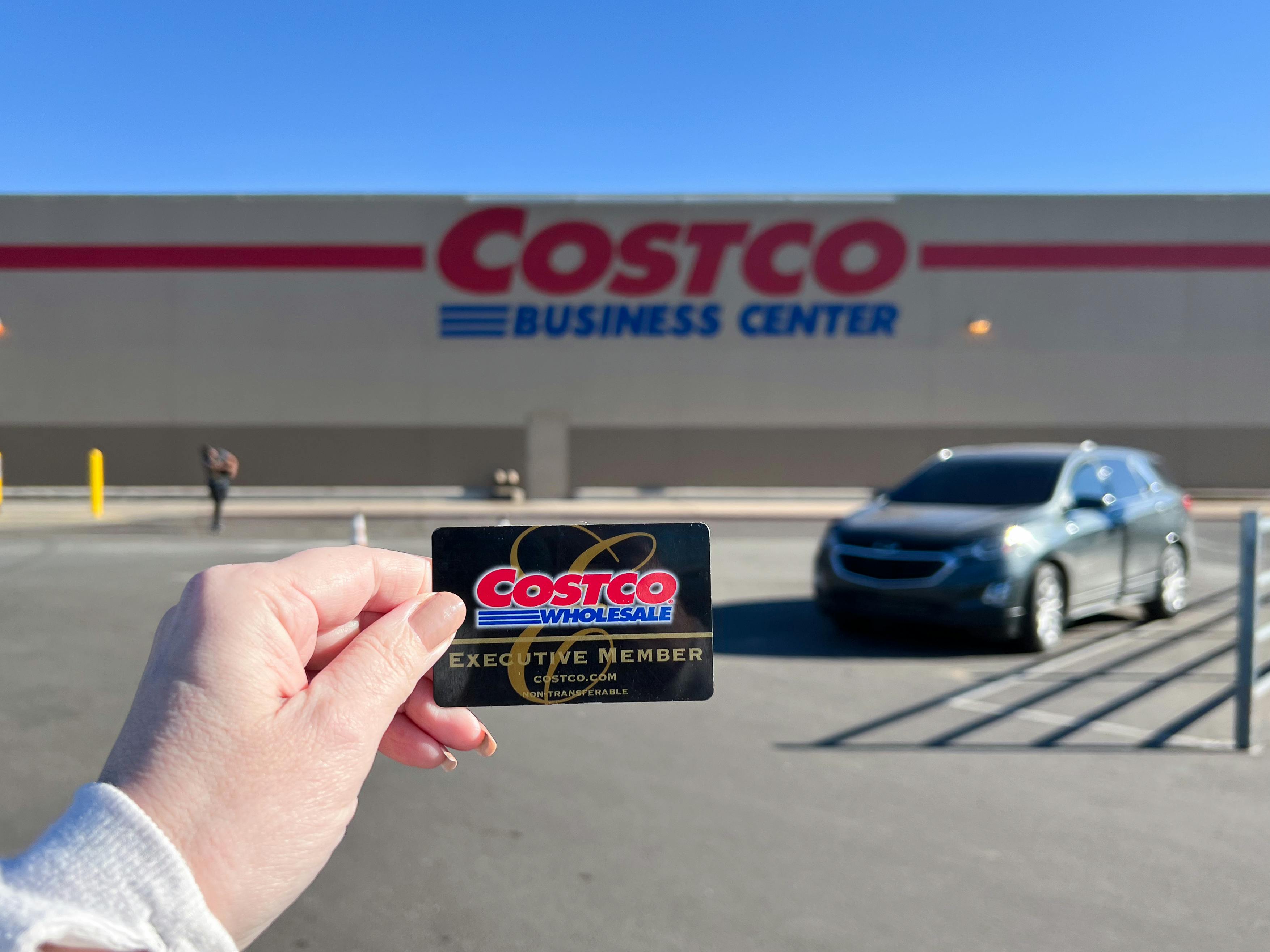 Someone holding up their Costco membership card in front of a Costco Business Center