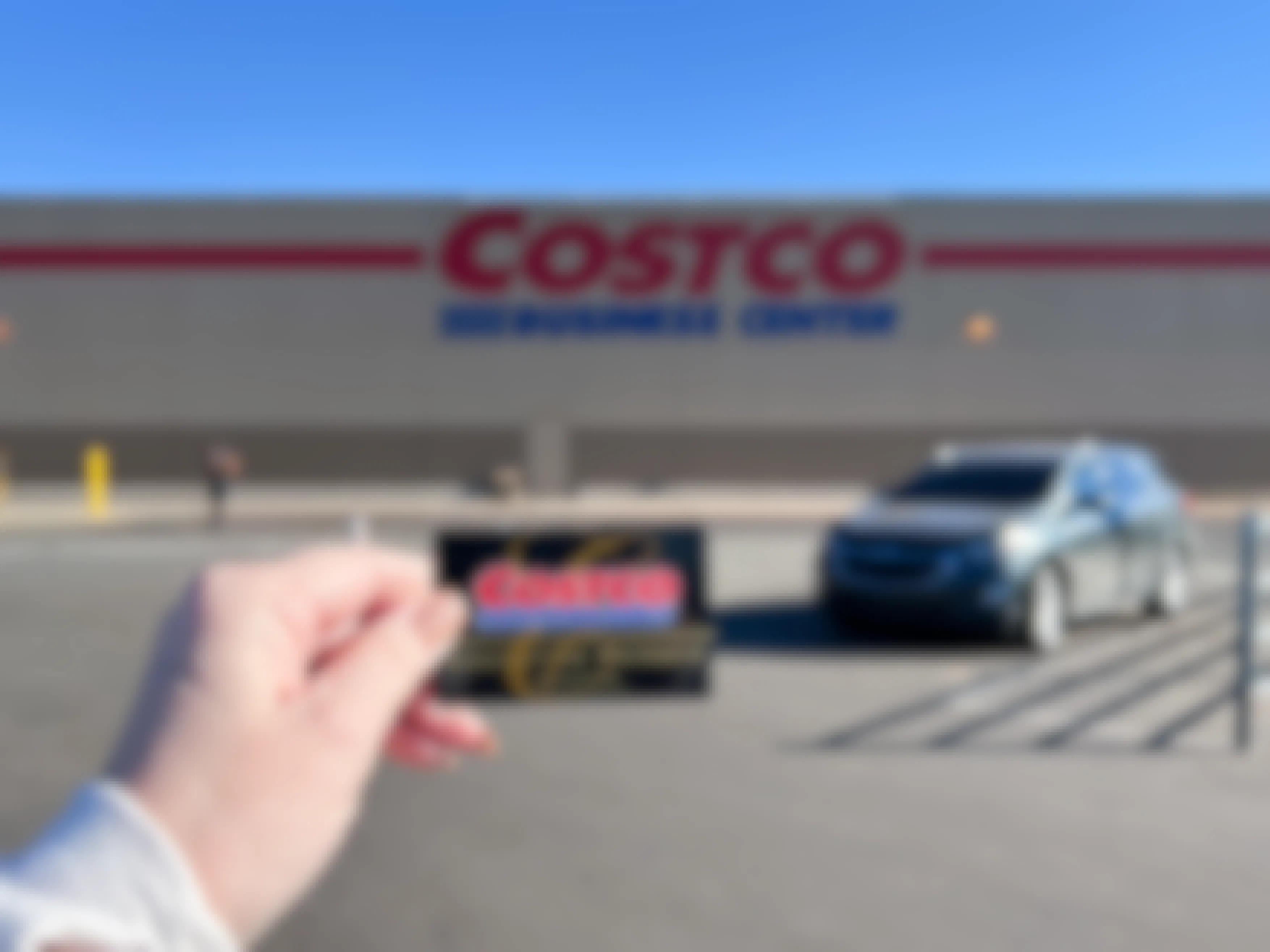 Someone holding up their Costco membership card in front of a Costco Business Center