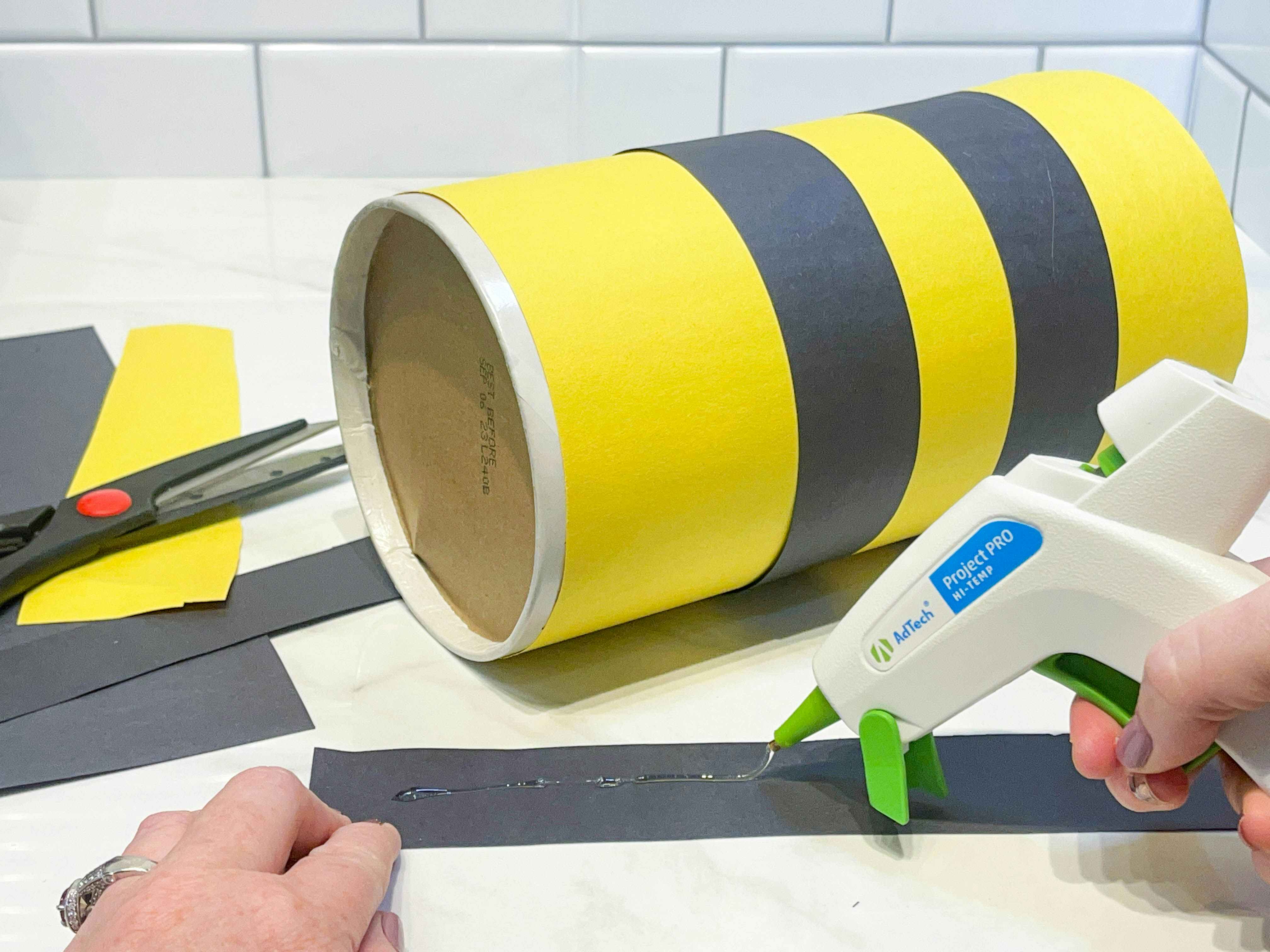 gluing strips of construction paper to a round container 