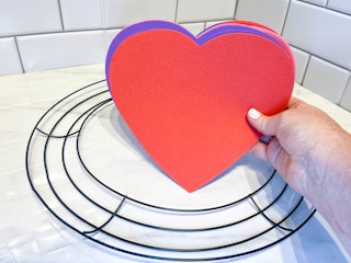 a person holding foam hearts being held in front of a wreath form