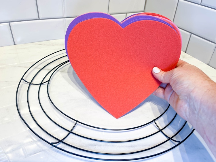a person holding foam hearts being held in front of a wreath form 