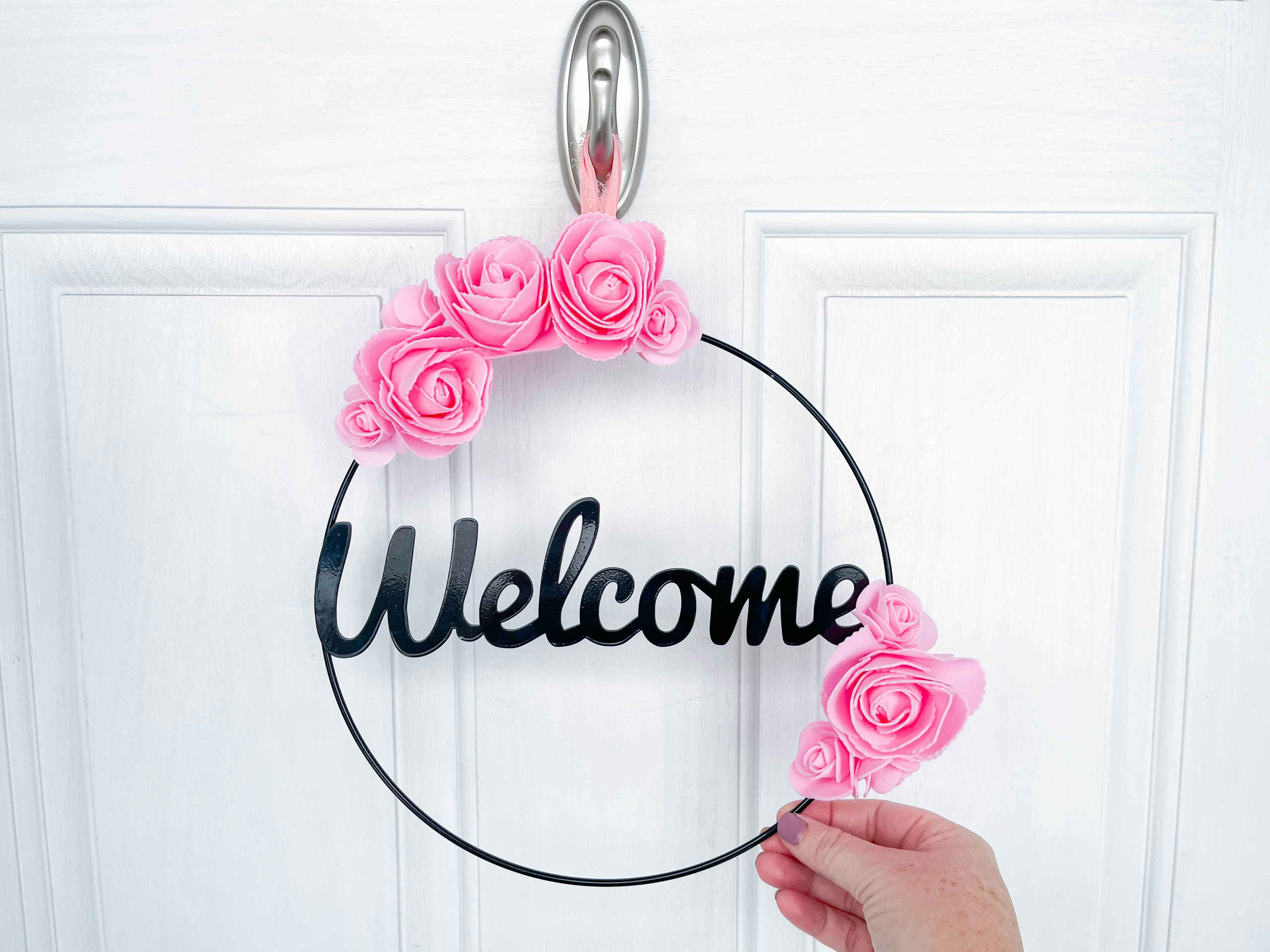 a welcome wreath with foam roses attached being held on a door 