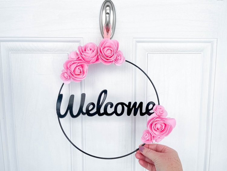 a welcome wreath with foam roses attached being held on a door 