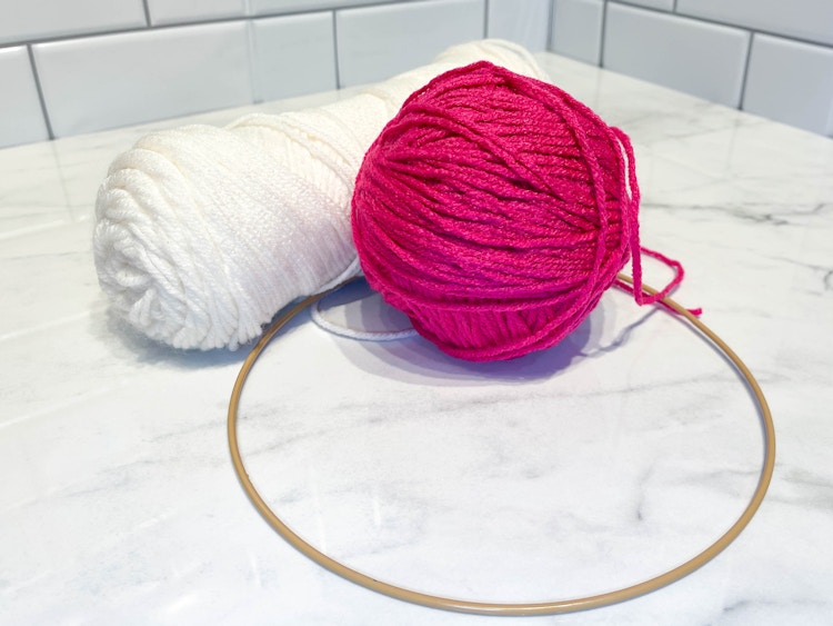 two colors of yarn sitting on a counter next to a hoop wreath 