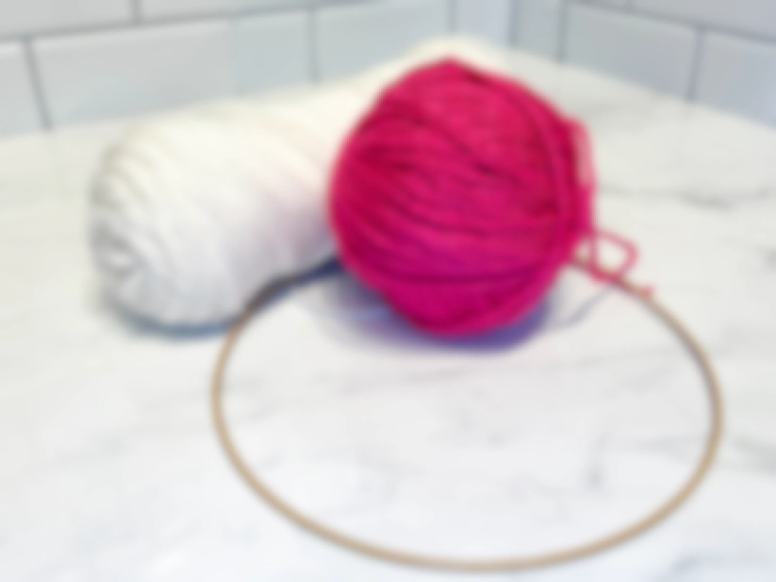 two colors of yarn sitting on a counter next to a hoop wreath 