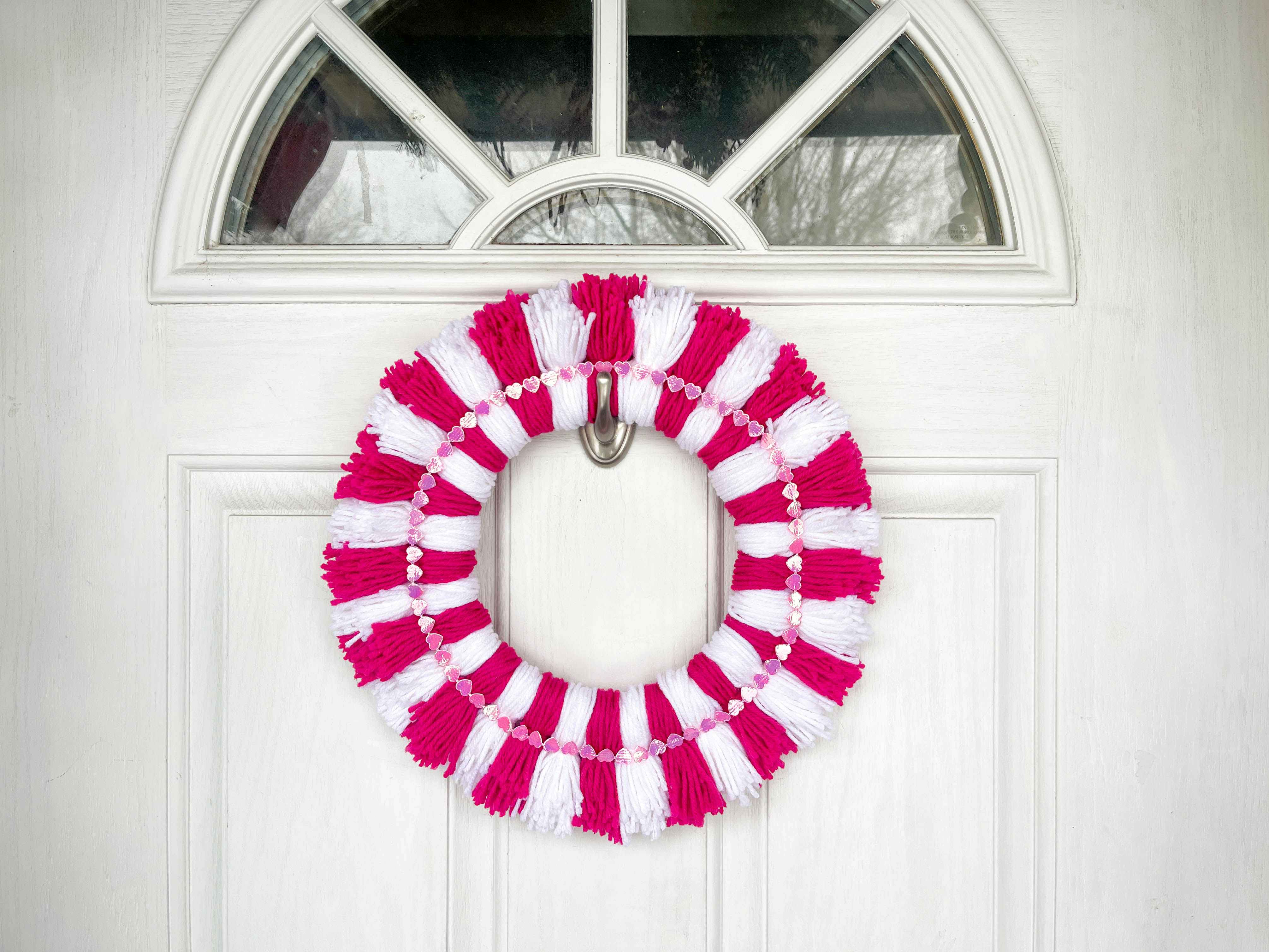 a diy yarn pom pom wreath hanging on a door