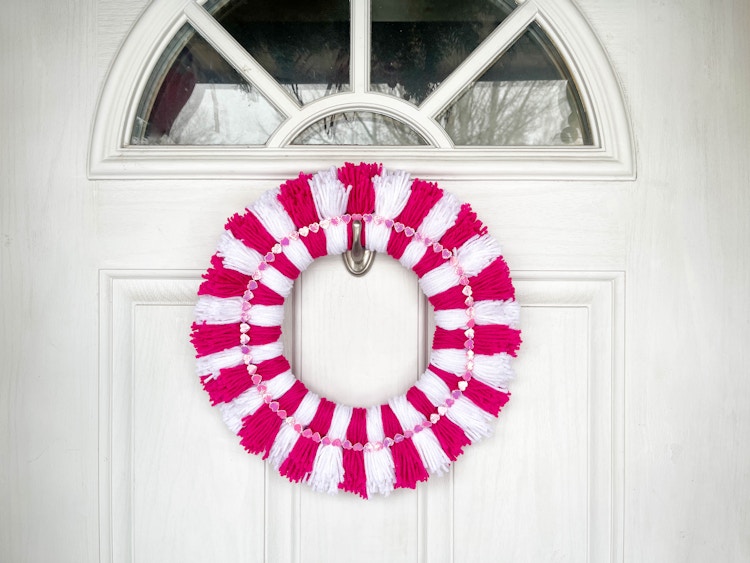a diy yarn pom pom wreath hanging on a door