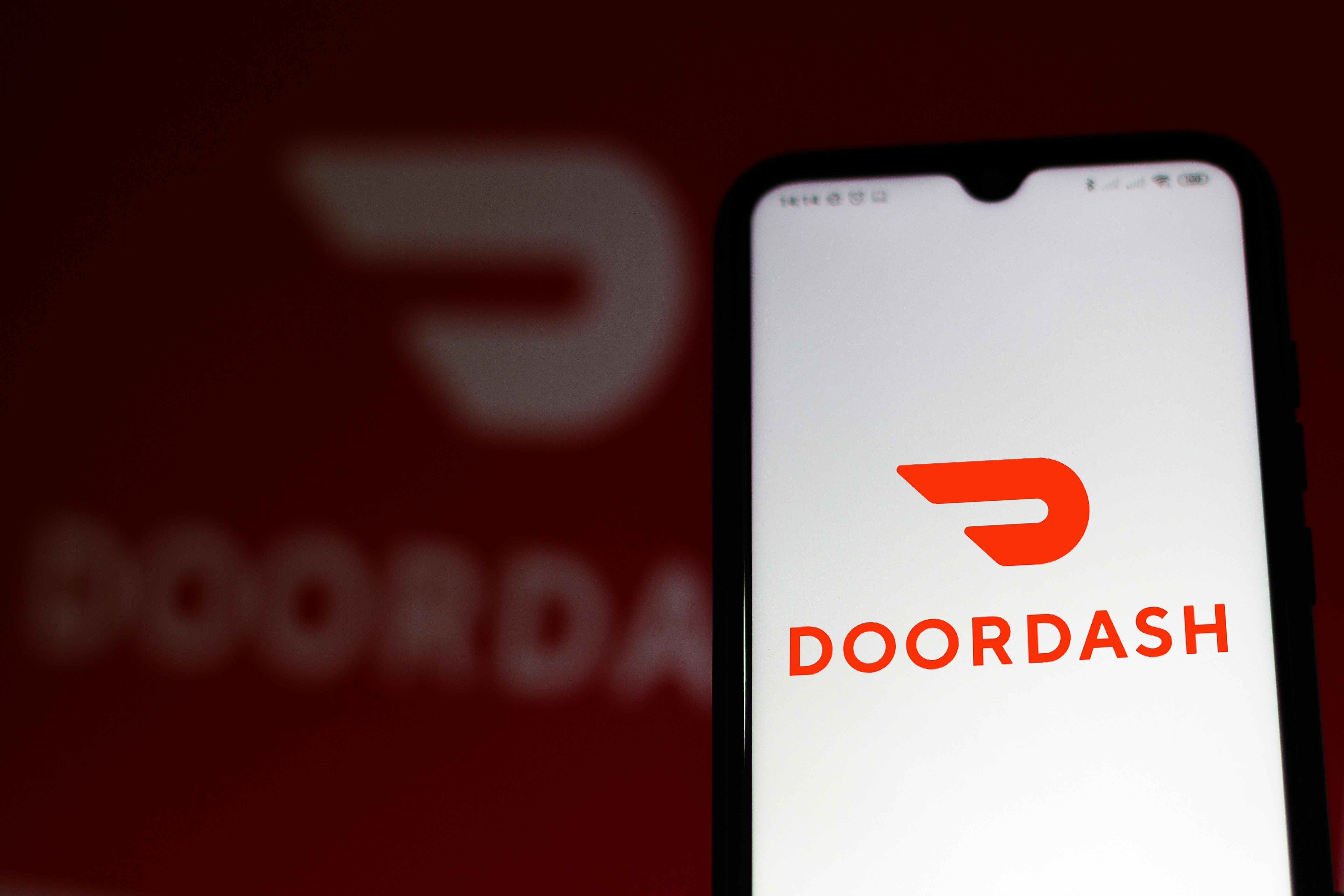A phone held up showing the doordash app intro image with the doordash logo shown largely in the background of the phone