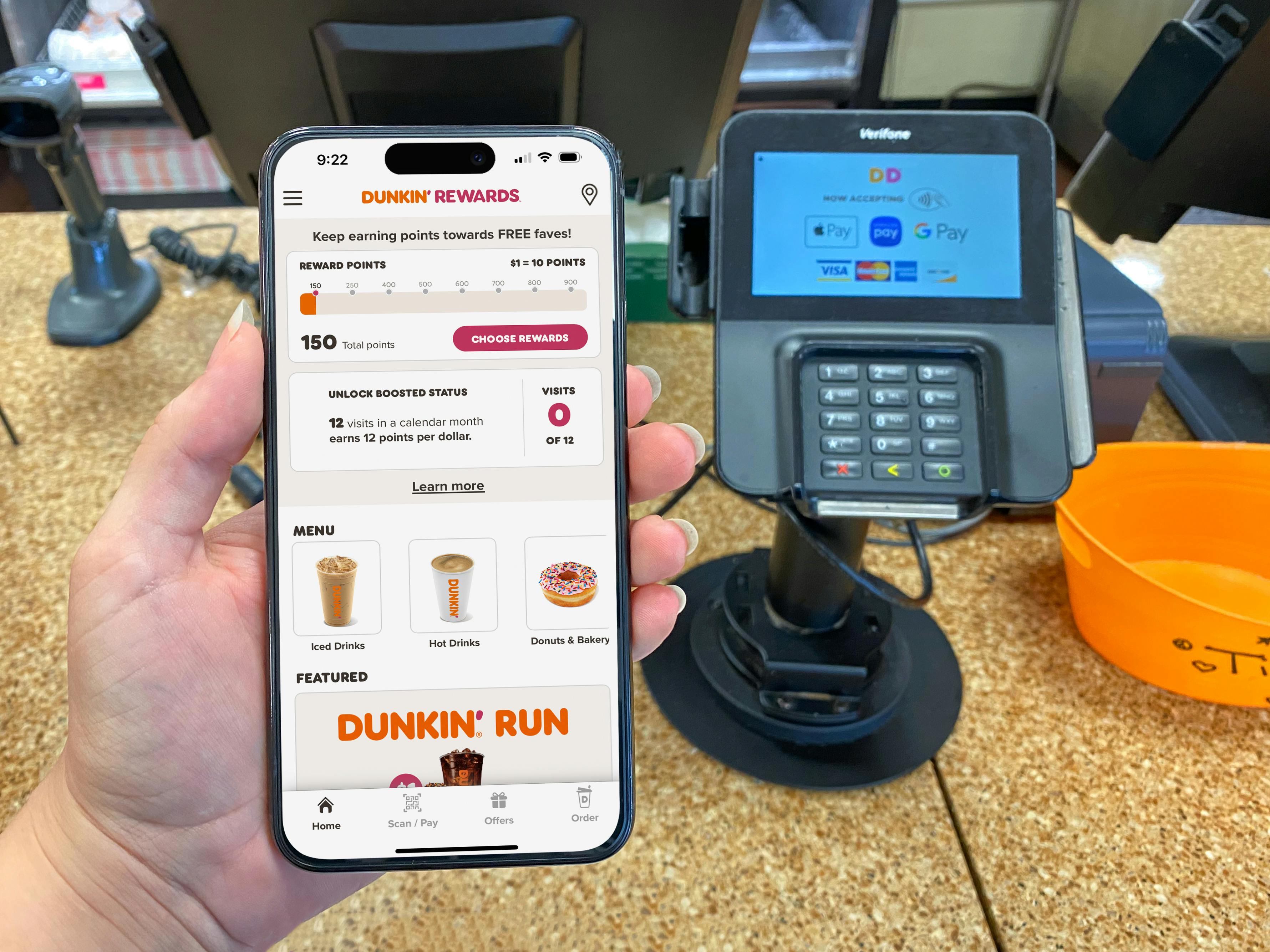 Someone looking at their phone displaying the Dunkin Rewards app at the counter inside a Dunkin