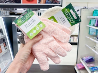 A couple of ecoTools bath gloves held out by hand in front of a store aisle.