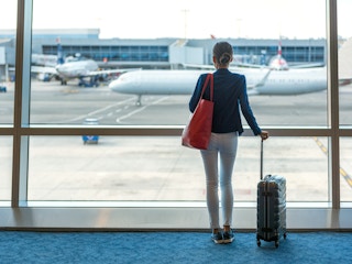 person with luggage looking out airport window at planes