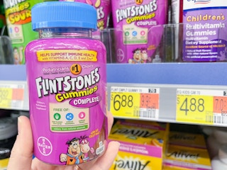 A Flintstones Gummies bottle held out by hand in front of a price sticker attached to a store shelf.