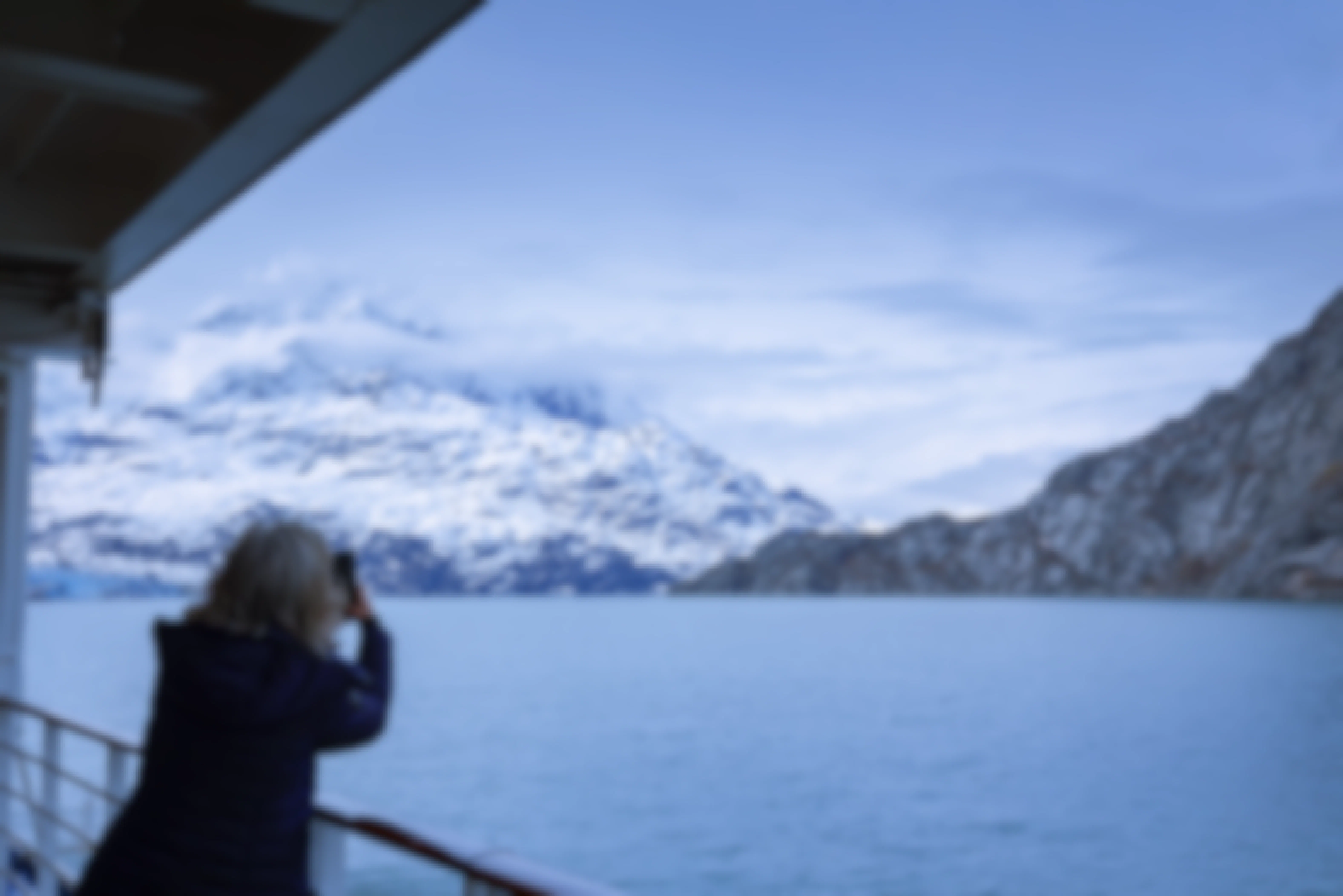 a woman leaning over the side of a boat to take a picture of a Glacier Bay National Park landscape in Alaska