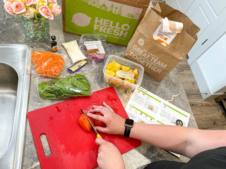 a person cutting up a tomato with a hello fresh kit on counter 
