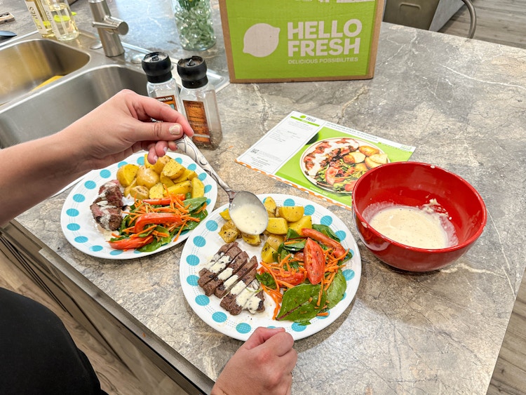 steak and potatoes meal on plate witha person adding a sauce on the meat