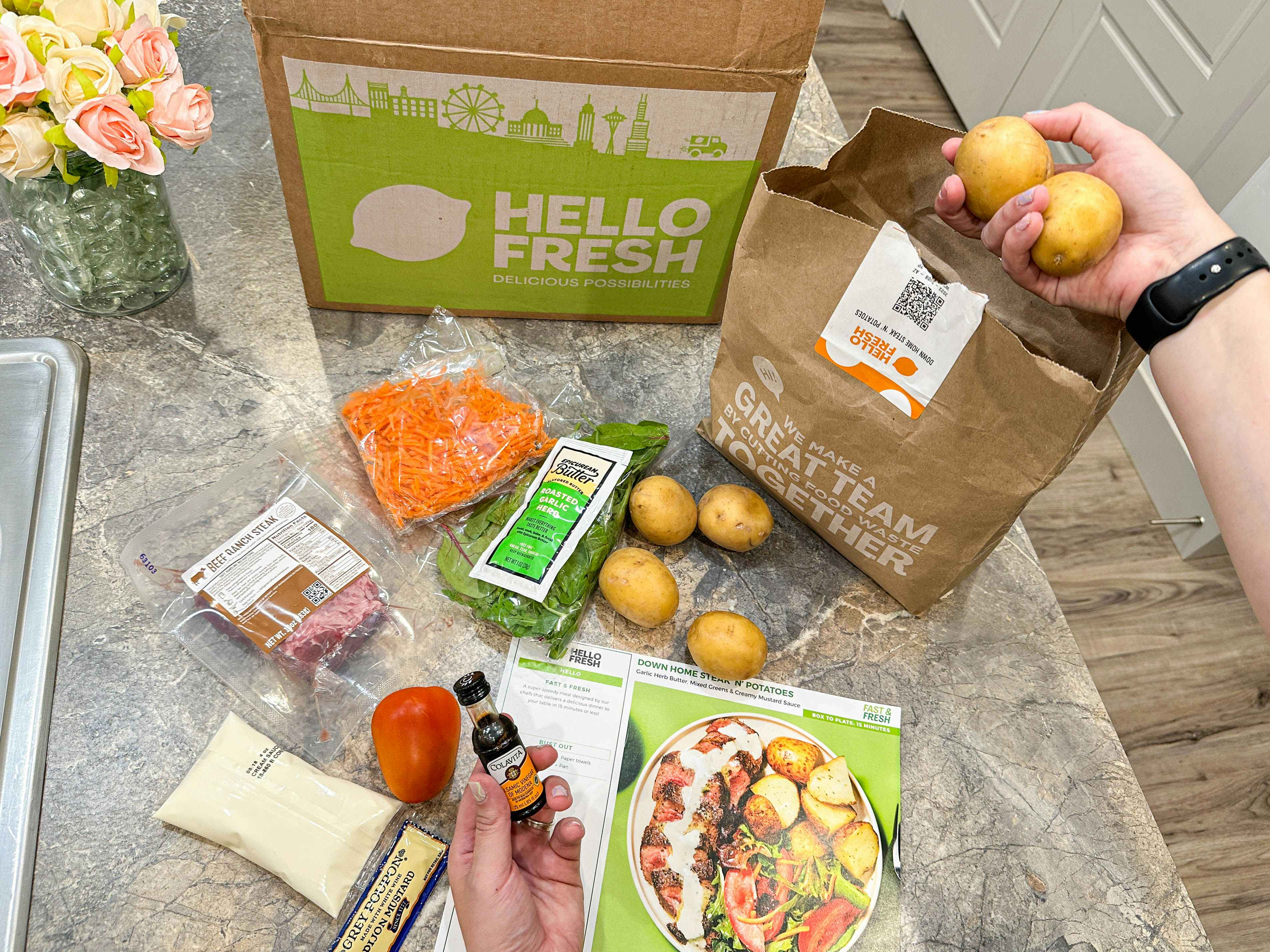 a hello fresh meal kit and ingredients on kitchen counter with potaotes being pulled out of a bag 