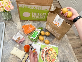 a hello fresh meal kit and ingredients on kitchen counter with potaotes being pulled out of a bag 