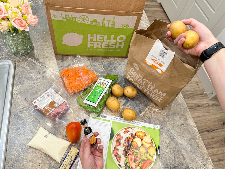 a hello fresh meal kit and ingredients on kitchen counter with potaotes being pulled out of a bag 